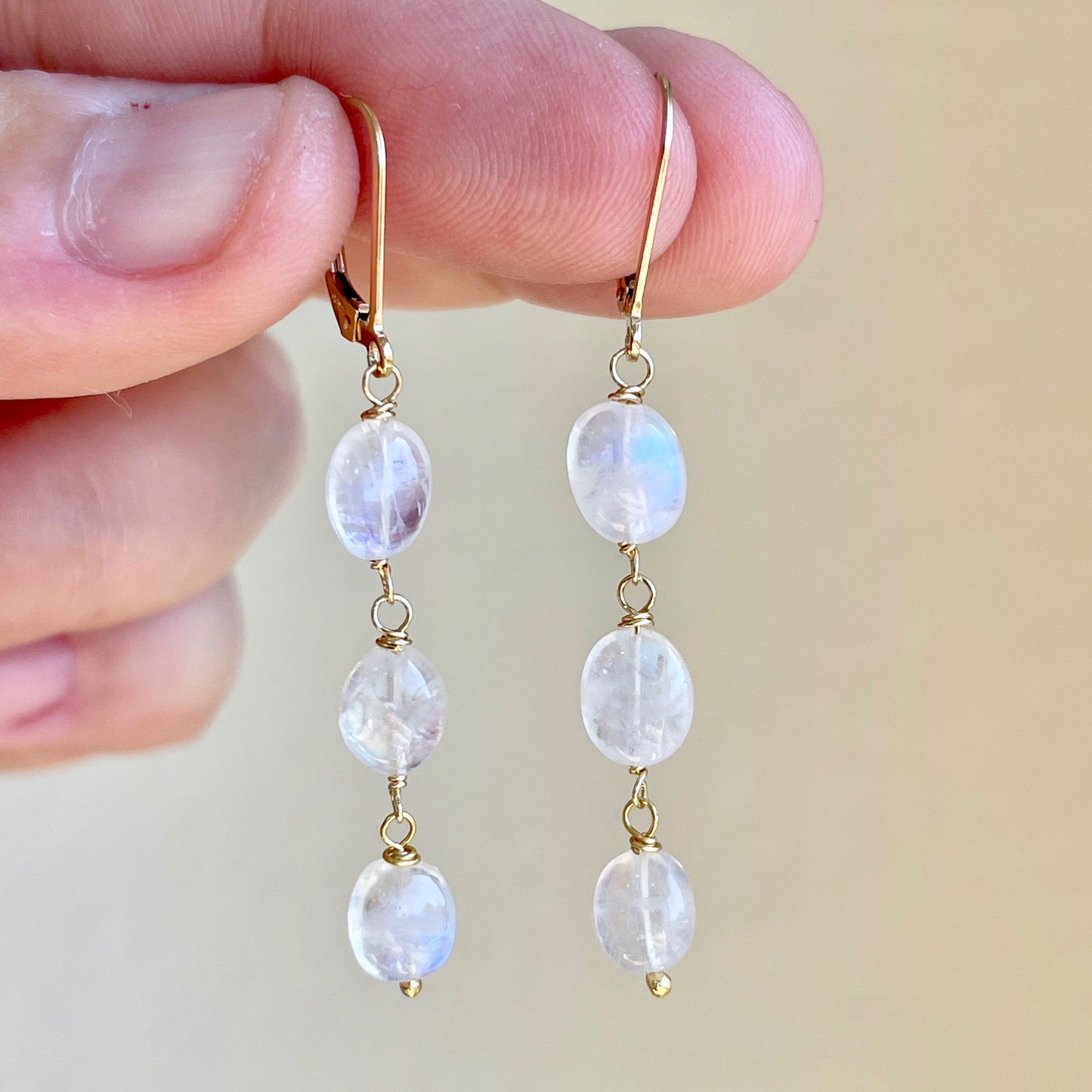 A pair of Rainbow Moonstone earrings with elongated ovals wire wrapped in gold filled wires, suspended from lever back wires.