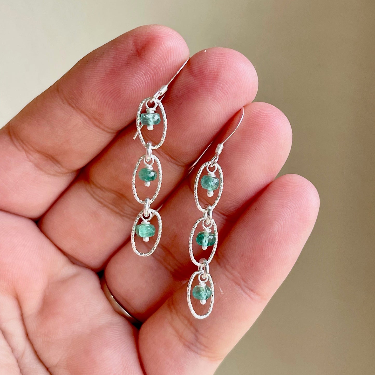 A pair of dainty green emerald earrings with gold ear wires and suspended from gold-filled or sterling silver oval links.