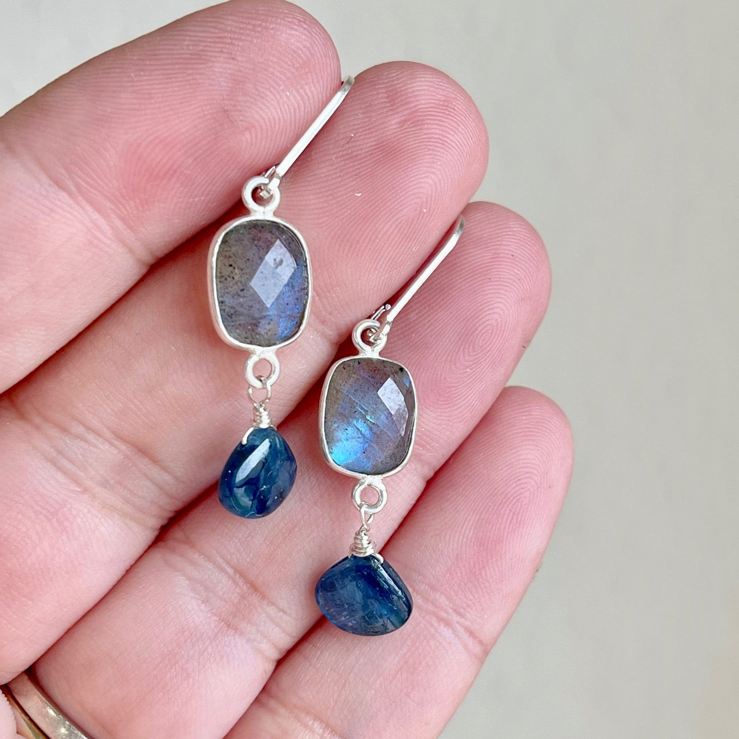 A pair of earrings featuring faceted green and blue labradorite rectangles bezel set in gold filled or sterling silver, suspended from lever back ear wires.