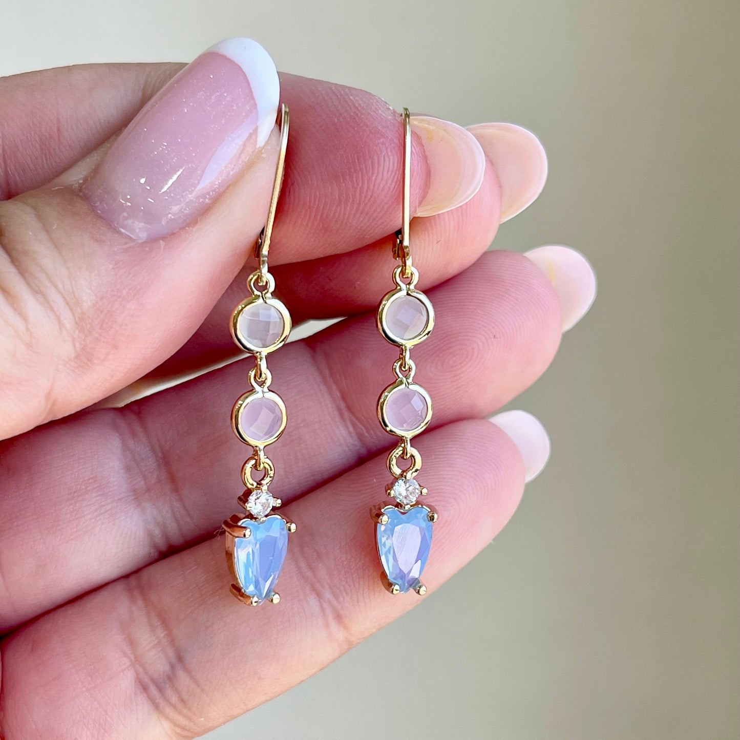 Gold earrings with pink and purple gemstones held by a hand against a neutral background