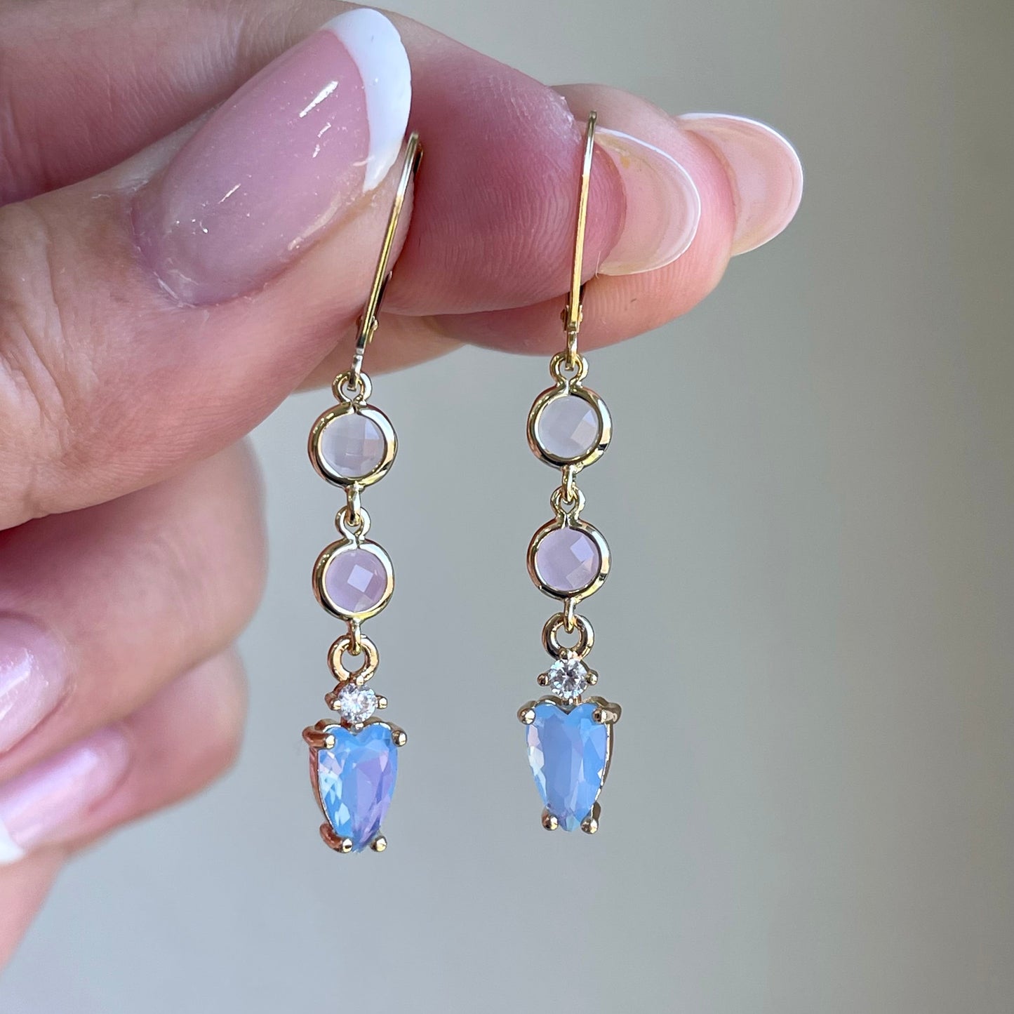 Gold earrings with gemstones held by a hand against a neutral background