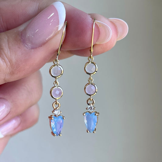 Gold earrings with gemstones held by a hand against a neutral background