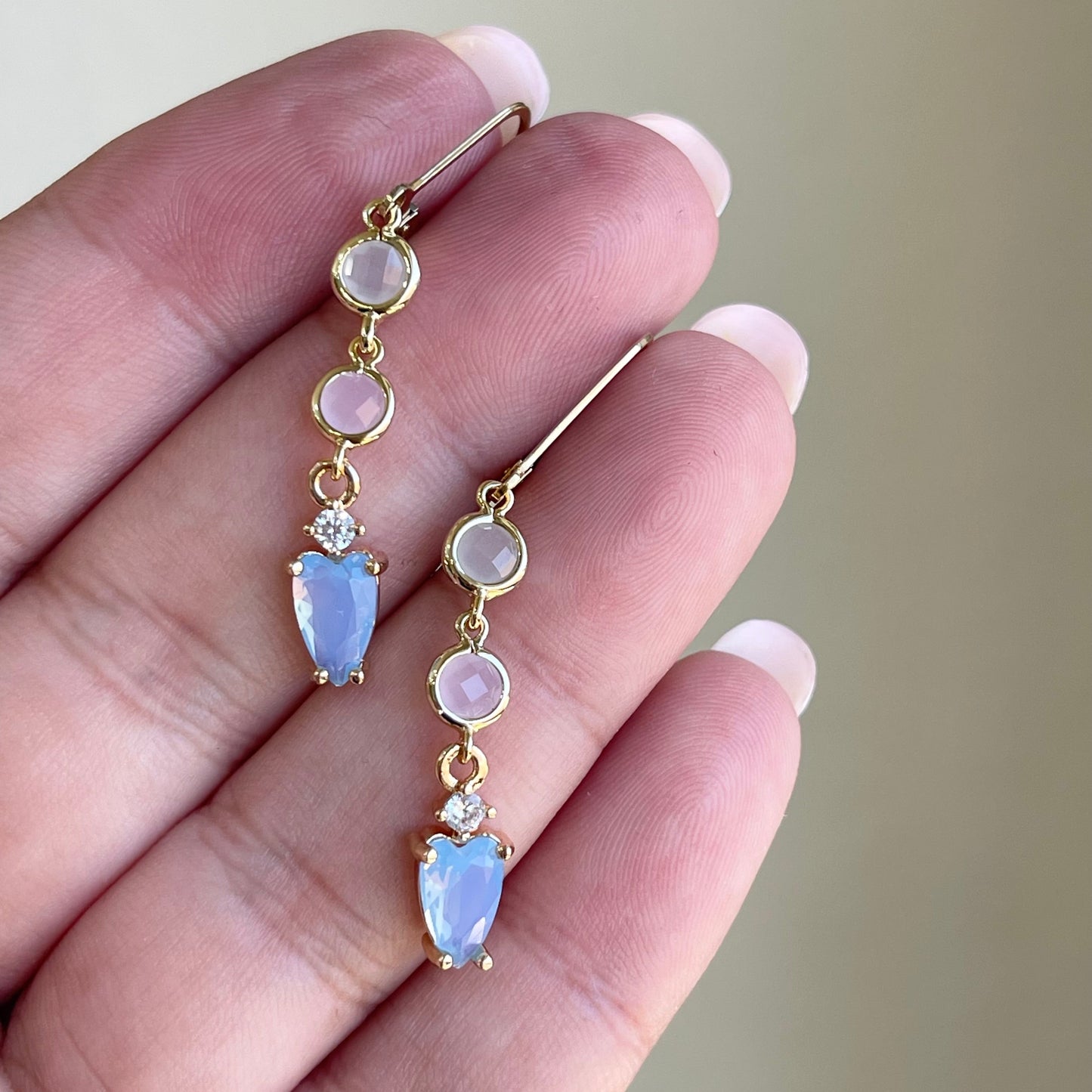 Gold earrings with gemstones held between fingers against a neutral background