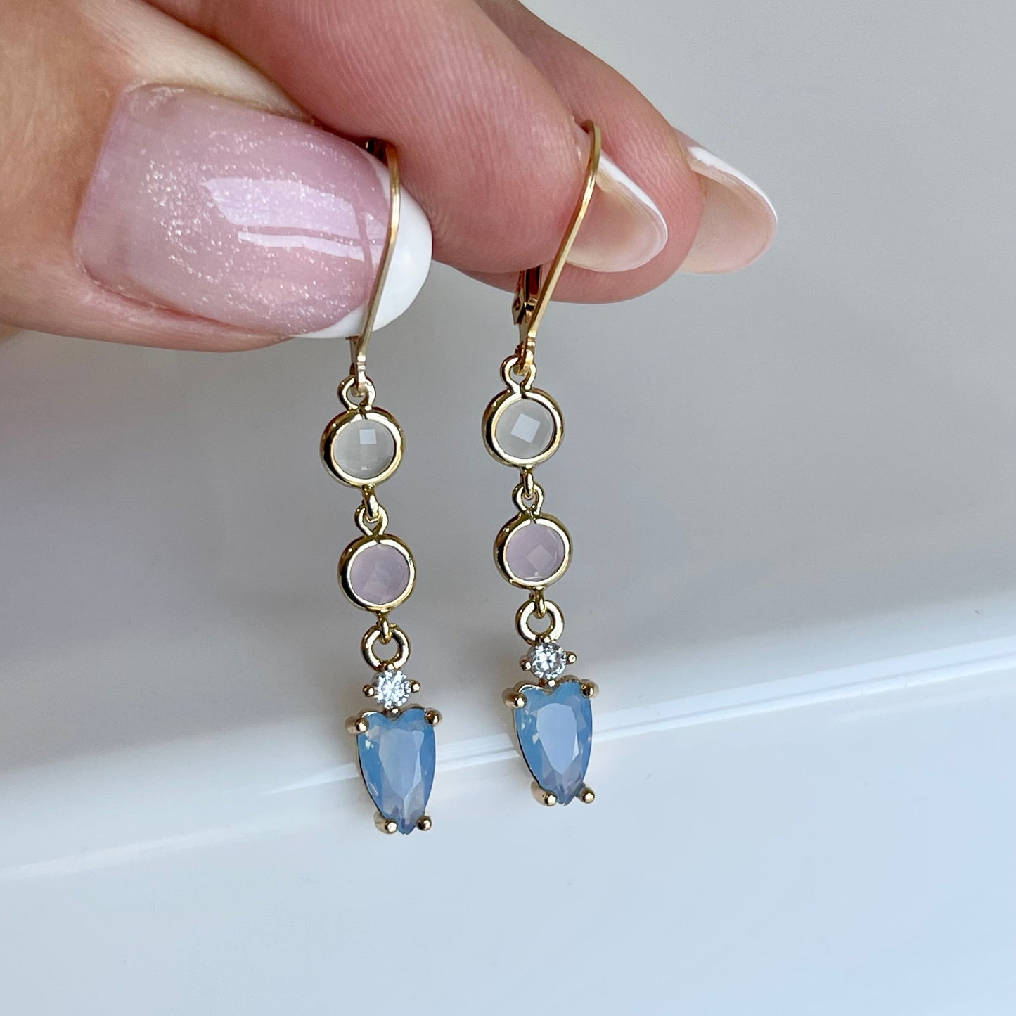 Gold earrings with blue gemstones held by a hand against a white background
